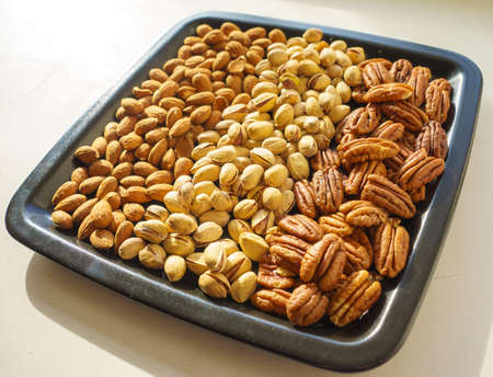 Nuts almonds, pistachios and pecans on a black plate, close-up, set.の写真素材