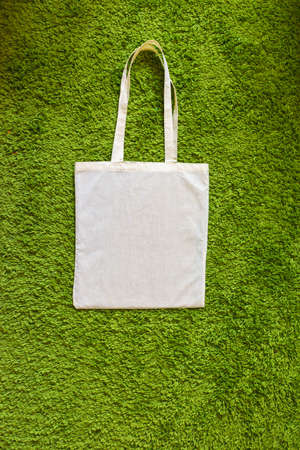 Eco bag made of unpainted 100 cotton on a green artificial grass background. Top view. Mockup