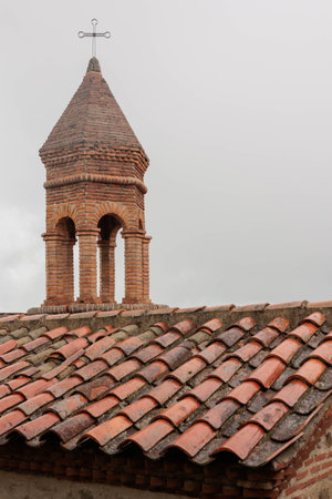 dome of the bell tower of the church in Sighnaghi. tiled roof in the foreground. There is a cloudy...
