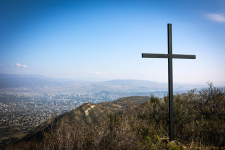 A metal cross on a hill near Tsodoreti overlooking Tbilisi and surrounding mountains under a clear blue sky, symbolizing peace and spirituality in a serene autumn landscapeの写真素材