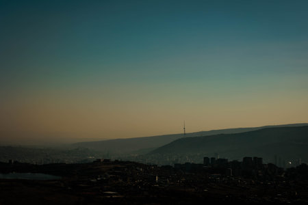 Silhouette of Tbilisi city at dusk with a view of the iconic TV tower and surrounding hills. A...
