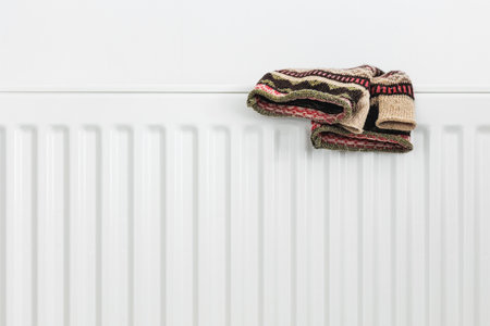 A white metal radiator with a folded knitted sweater on top. Cozy winter atmosphere, home heating concept. Warm and comfortable interior detail, minimalistic designの写真素材