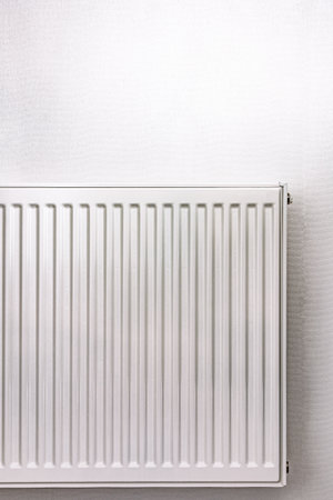 White metal radiator against a light wall. Minimalistic heating element in a modern interior. Clean and simple design with a neutral color paletteの写真素材