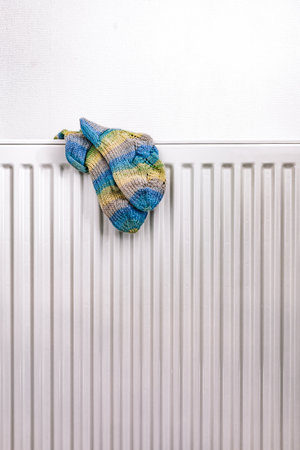 A pair of colorful knitted wool socks drying on a white radiator, evoking a sense of warmth, home comfort, and cozy winter vibes. The soft texture and striped pattern add a touch of seasonal charmの写真素材