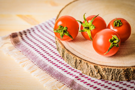 Fresh cherry tomatoes on a rustic wooden cutting board with a checkered towel. A cozy food composition emphasizing organic produce, natural ingredients, and a farmhouse-style kitchen settingの写真素材