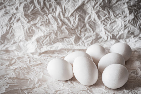 White eggs arranged on crumpled paper, creating a clean and organic composition. Soft natural light...