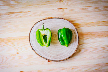Fresh green bell pepper on a rustic wooden board. Vibrant color and natural texture emphasize...