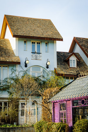 Charming countryside house with a wooden shingle roof and a whimsical purple garden house. Sunlight enhances the textures of the rustic architecture and lush greeneryの写真素材