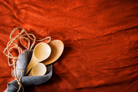 Rustic wooden spoons wrapped in a gray napkin with natural jute twine on a textured red fabric background. Eco-friendly kitchen concept with warm, earthy tones and a handmade aestheticの写真素材