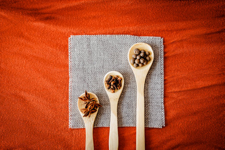 Top view of star anise, cloves, and all spice in wooden spoons on linen cloth and orange background. Warm, rustic mood for fall recipes, natural cooking and food blog contentの写真素材