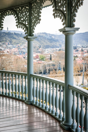 Beautiful traditional Georgian balcony with carved wooden elements and panoramic view of Tbilisi old town and hills. Calm spring mood and historic architectureの写真素材