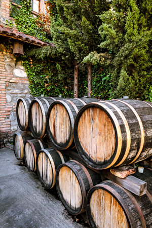 Wooden wine barrels stacked in a traditional Georgian winery courtyard, surrounded by ivy-covered...