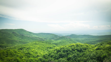 Vast green hills and a hidden lake under a clear sky in the Georgian countryside. Peaceful and expansive natural landscape from a high vantage pointの写真素材