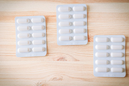 Flat lay of white capsule medicine packs arranged diagonally. Clean pharmaceutical image with wooden texture, ideal for health-related visualsの写真素材
