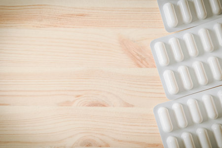 Full blister packs of white medical capsules on wooden background. Minimalist flat lay of pharmaceutical treatment, healthcare or medication concept in natural lightの写真素材