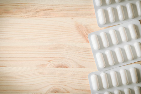 Full blister packs of white medical capsules on wooden background. Minimalist flat lay of pharmaceutical treatment, healthcare or medication concept in natural lightの写真素材
