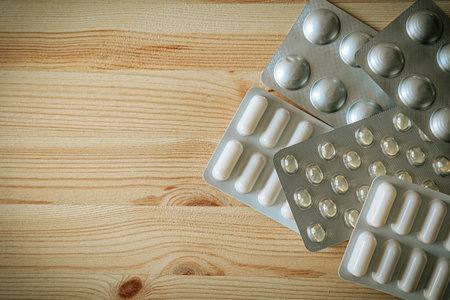 Flat lay of various blister packs with softgel capsules and pills. Natural light and wooden surface...