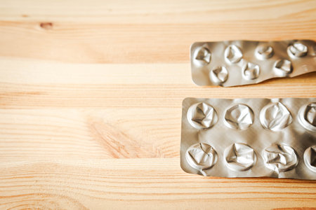 Empty blister packs of pills on light wooden table in natural daylight. Concept of finished treatment, medication use, or pharmaceutical waste. Minimalist healthcare sceneの写真素材