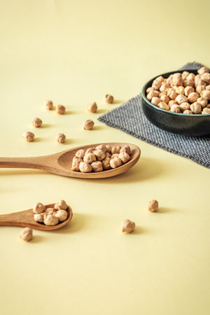 Minimalist composition with chickpeas in wooden spoons and ceramic bowl on warm pastel background. Healthy and natural food conceptの写真素材