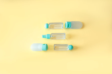 Neatly aligned flat lay of transparent and silicone travel bottles on pastel yellow background....