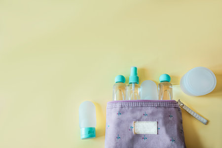 Flat lay of a purple toiletry bag filled with travel-size cosmetic bottles on a soft yellow...
