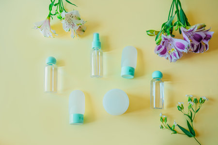 Flat lay of travel cosmetic bottles arranged symmetrically with blooming flowers on pastel background. Clean, soft, and elegant design for beauty, skincare, or summer wellnessの写真素材