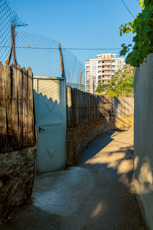 Narrow Tbilisi street with rustic wooden fence, metal door, and modern apartment building in the...