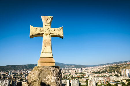 Stone cross monument overlooking Tbilisi city under bright sunlight, symbolizing faith and culture in Georgiaの写真素材