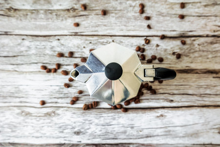 Top-down shot of a classic aluminum moka pot on a rustic wooden table scattered with coffee beans, conveying cozy morning vibes and slow-living homebrew cultureの写真素材