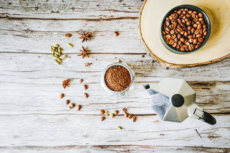 Rustic coffee still life: ground arabica, moka pot and bowl of beans on raw wood slice with...