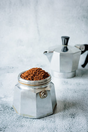 Freshly ground coffee fills the bottom chamber of a classic stovetop moka pot on a light concrete surface, evoking a calm, minimalist morning kitchen moodの写真素材