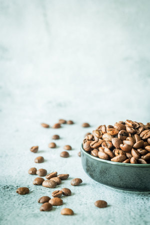 Shallow-depth vertical still life with roasted coffee beans in a charcoal ceramic bowl and a blurred...