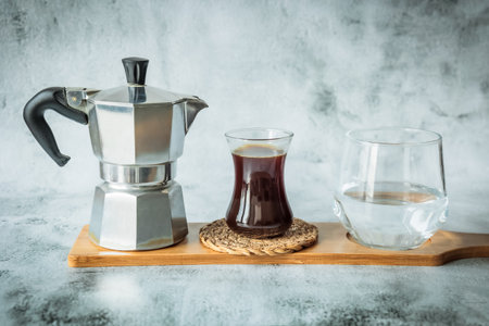 Classic moka pot, freshly brewed black coffee in a slim glass and clear water in a tumbler lined up...