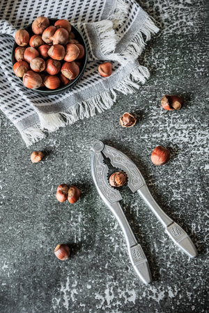 Overhead layout: hazelnuts in bowl on fringed towel with nutcracker and loose nuts over distressed...