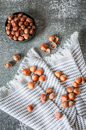 Overhead composition: hazelnuts spilling across checked kitchen towel on weathered slate background,...