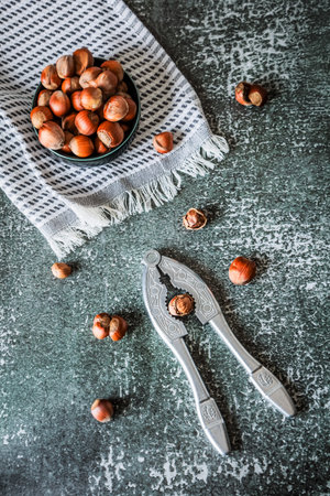 Overhead layout: hazelnuts in bowl on fringed towel with nutcracker and loose nuts over distressed...
