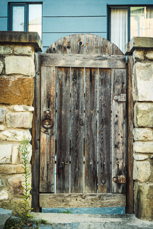 Old wooden gate with iron handle set in a rustic stone wall, captured in Mtskheta, Georgia. Natural textures of aged wood and rough masonry in warm afternoon lightの写真素材