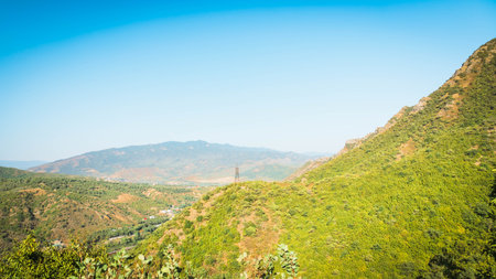 Mountain valley near Mtskheta, Georgia, seen from above. A single power line tower stands among green hills, contrasting with the vast natural landscape and distant peaksの写真素材