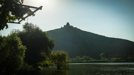 Silhouette of Jvari Monastery on a hill above Mtskheta, Georgia, at sunrise with calm river and soft...