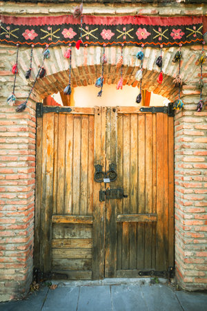 Rustic wooden gate with traditional Georgian wool tassels and brick arch in Mtskheta, Georgia....