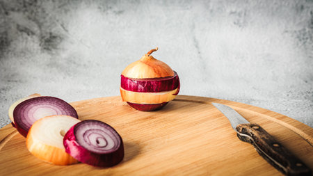Sliced hybrid onion made from red and yellow layers, placed beside onion rings and rustic knife on...