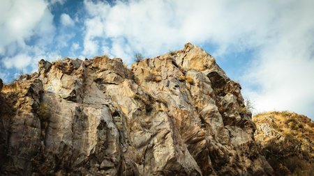 Sharp rocky cliffs rise against a partly cloudy sky in Armenia. A dramatic view of textured stone formations lit by warm sunlight, capturing raw and wild natural beautyの写真素材