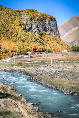 Vertical view of a turquoise mountain river flowing through a rural village near Truso Gorge, Georgia. Autumn forest and dramatic cliffs frame this peaceful landscapeの写真素材