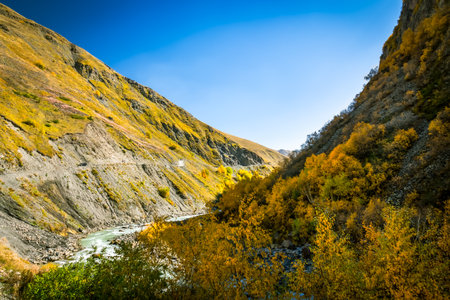 Winding road along steep, dry mountain slopes of Truso Valley in Georgia during autumn. A remote and scenic travel route through the wild Caucasus terrainの写真素材