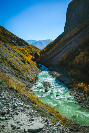 Mountain river with turquoise water cutting through steep cliffs and autumn forest in Truso Valley, Georgia. Deep shadows and glowing trees create a dramatic and wild atmosphereの写真素材
