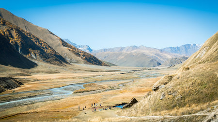 Truso Valley in Georgia in early autumn. Golden trees, turquoise river, and dramatic mountain peaks under clear blue skies create a sense of peace, freedom, and untouched natureの写真素材