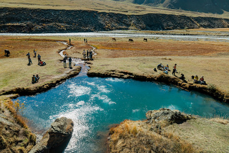 Travelers explore a bubbling mineral lake in Truso Valley, Georgia, surrounded by autumn mountains. A popular hiking spot with surreal turquoise water and peaceful sceneryの写真素材
