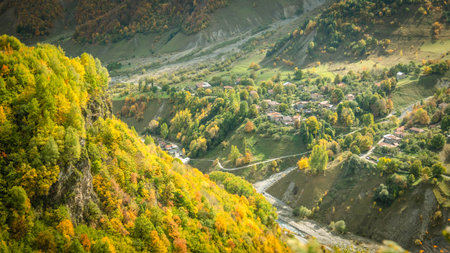 Aerial view of a small mountain village in Georgia surrounded by vibrant autumn foliage. Peaceful...