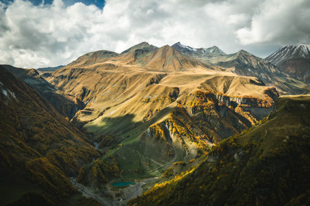 Majestic autumn landscape of the Caucasus mountains in Georgia with golden slopes and a small turquoise lake in the valley. Dramatic light and vibrant colors of untouched natureの写真素材