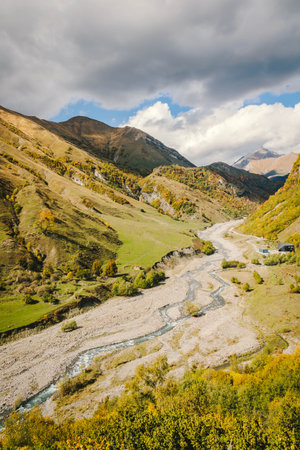 Panoramic autumn view of a winding river in the mountains. Vibrant foliage, rugged hills, and dramatic skies create a peaceful and remote highland landscapeの写真素材